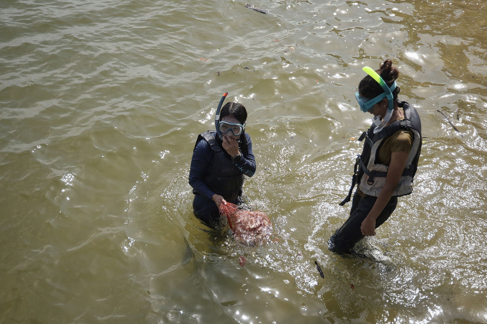 Ecologist Yukie Yokoyama (left) adjusting her snorkel before proceeding with project volunteer Nikita Choudhary (right) to secure a bag of oyster shells onto the pillars under the dock at Changi Sailing Club on Jan 27, 2024.