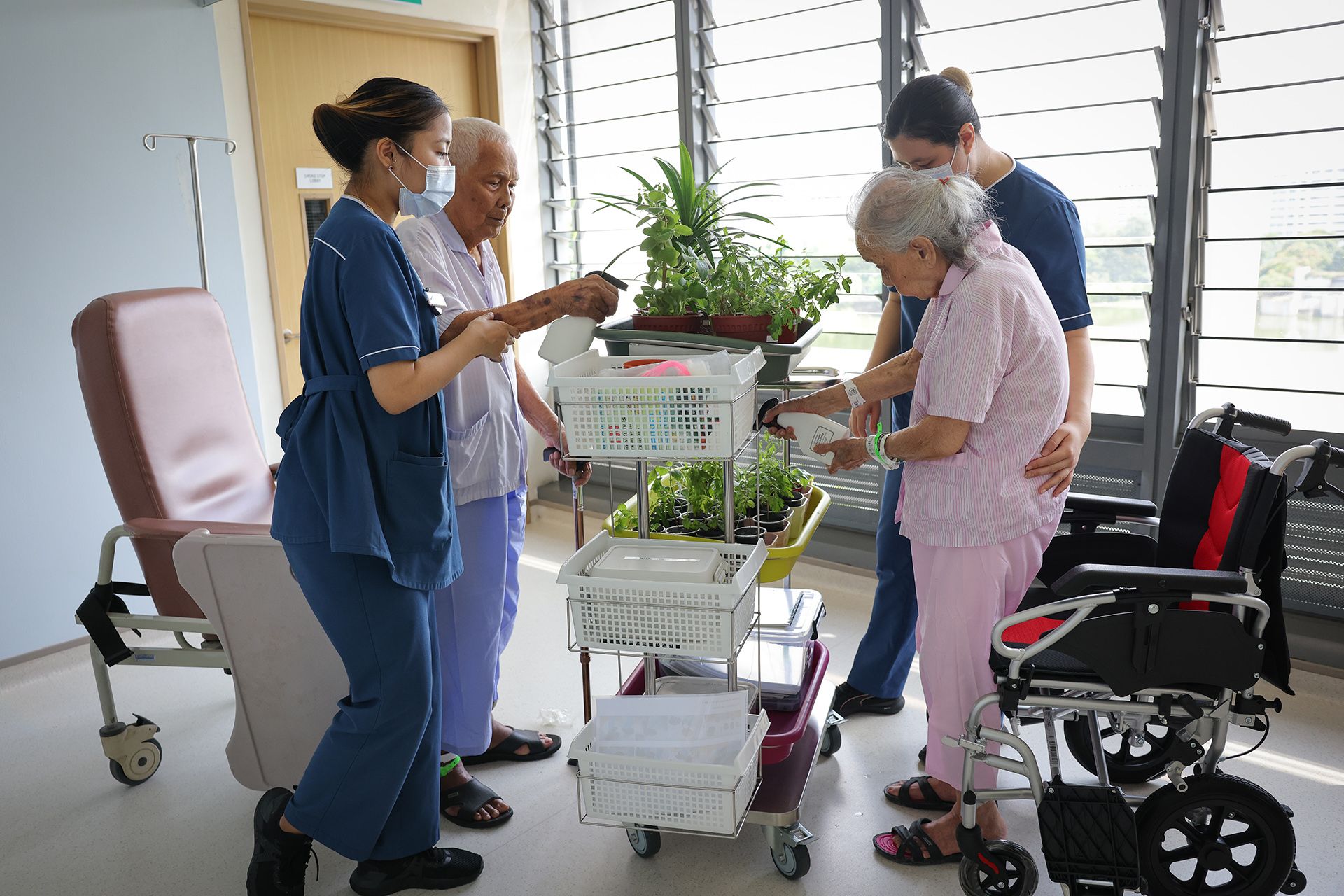Senior staff nurses Dian Azrinda (extreme left) and Gwen Huw (extreme right) assist patients Haji Saad and Pua Hor Lee in standing and watering plants. Encouraging patients to stand helps improve their physical condition.